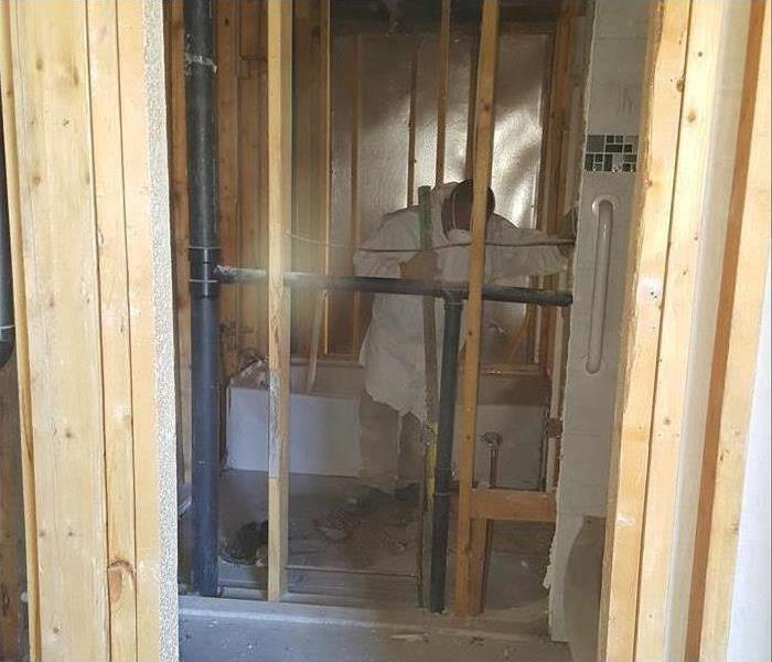 Wooden structure of a bathroom. There is technician wearing protective equipment and cleaning